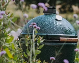The Big Green Egg surrounded by flowers and greenery.
