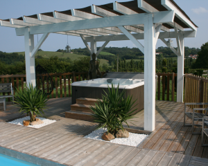 Outdoor hot tub installed on a patio underneath a pergola on a bright, sunny day.
